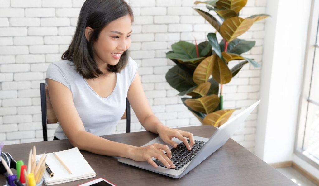 Portrait d'une belle femme asiatique souriante et heureuse utilisant la technologie d'un ordinateur portable tout en étant assis sur une table et en tapant sur le clavier